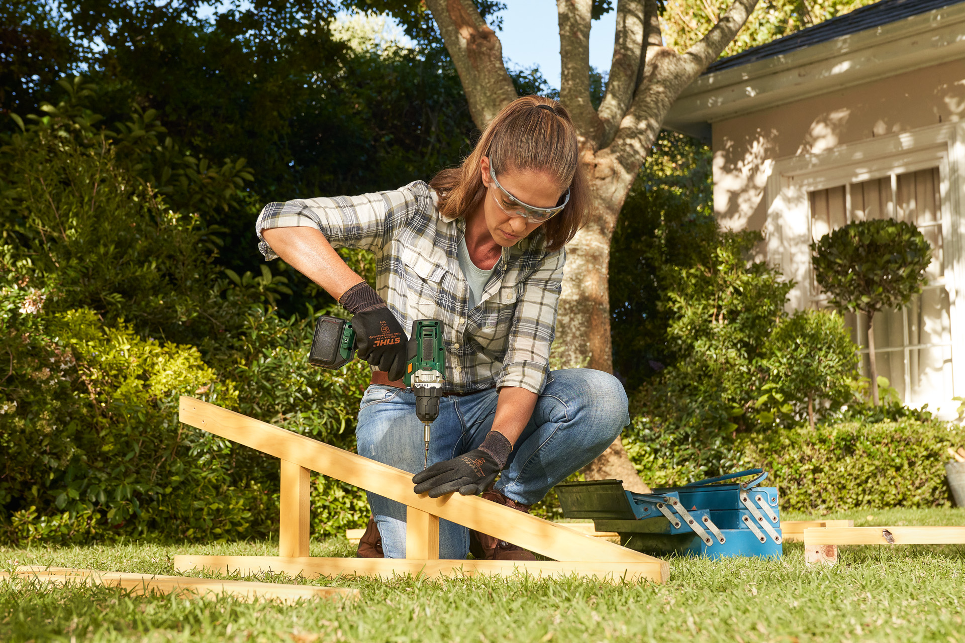 Një person i veshur me doreza mbrojtëse STIHL duke përdorur një trapano pa kabllo në një tra druri