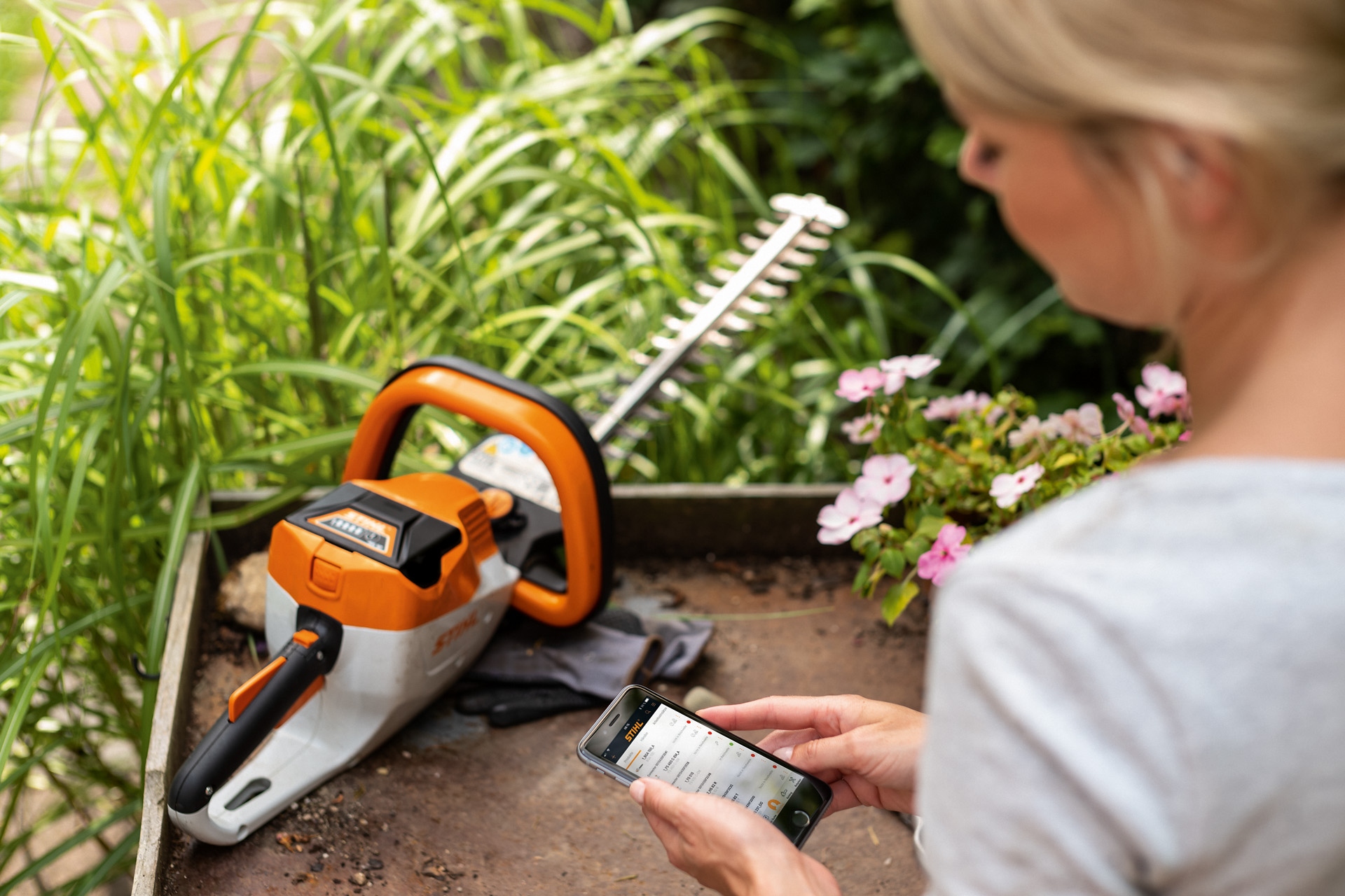 Një grua që regjistron makinën e saj të prerjes së gardheve STIHL duke përdorur aplikacionin STIHL në një telefon inteligjent