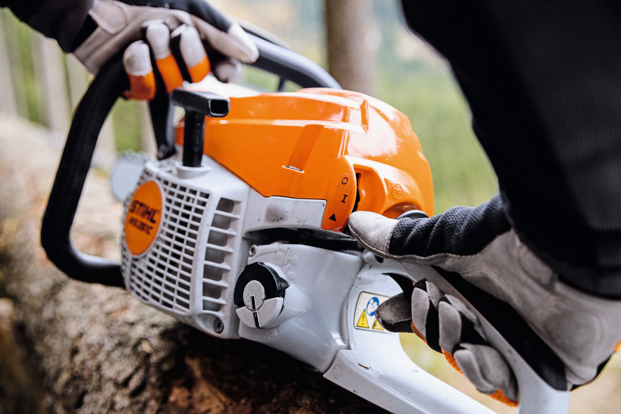 Pamje nga afër e një sharre motorike me benzinë ​​STIHL MS 261 CM që ndizet nga një person që mban doreza mbrojtëse.