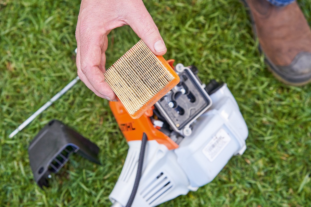 Një person që heq filtrin e ajrit nga një trimer STIHL për ta pastruar atë 