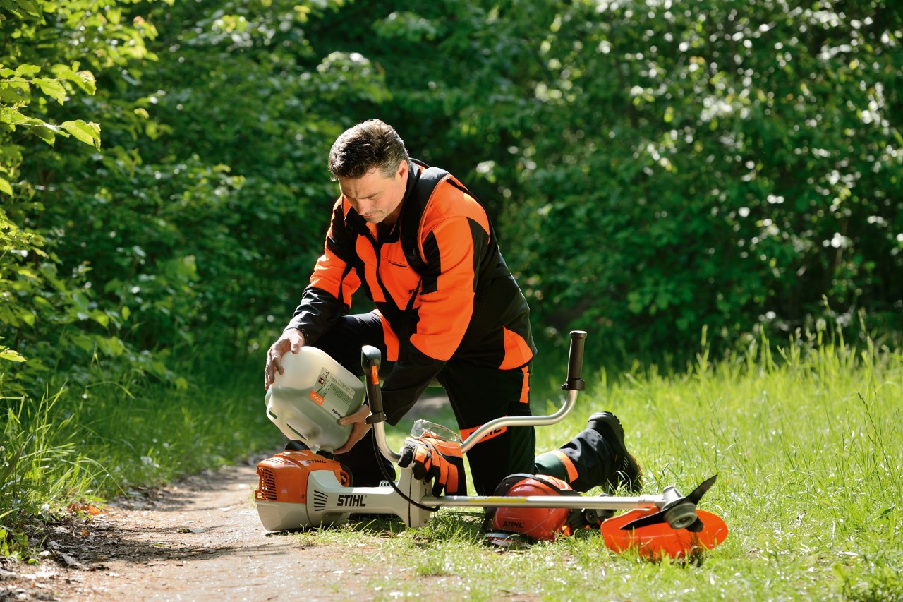 Një burrë i veshur me pajisje mbrojtëse STIHL duke mbushur me karburant një trimer STIHL me një përzierje benzine-vaji
