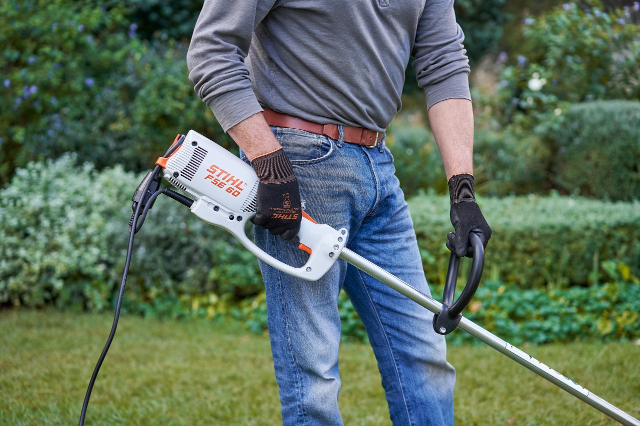 Një burrë që mban doreza mbrojtëse duke mbajtur motokosën elektrike STIHL FSE 60 me të dyja duart