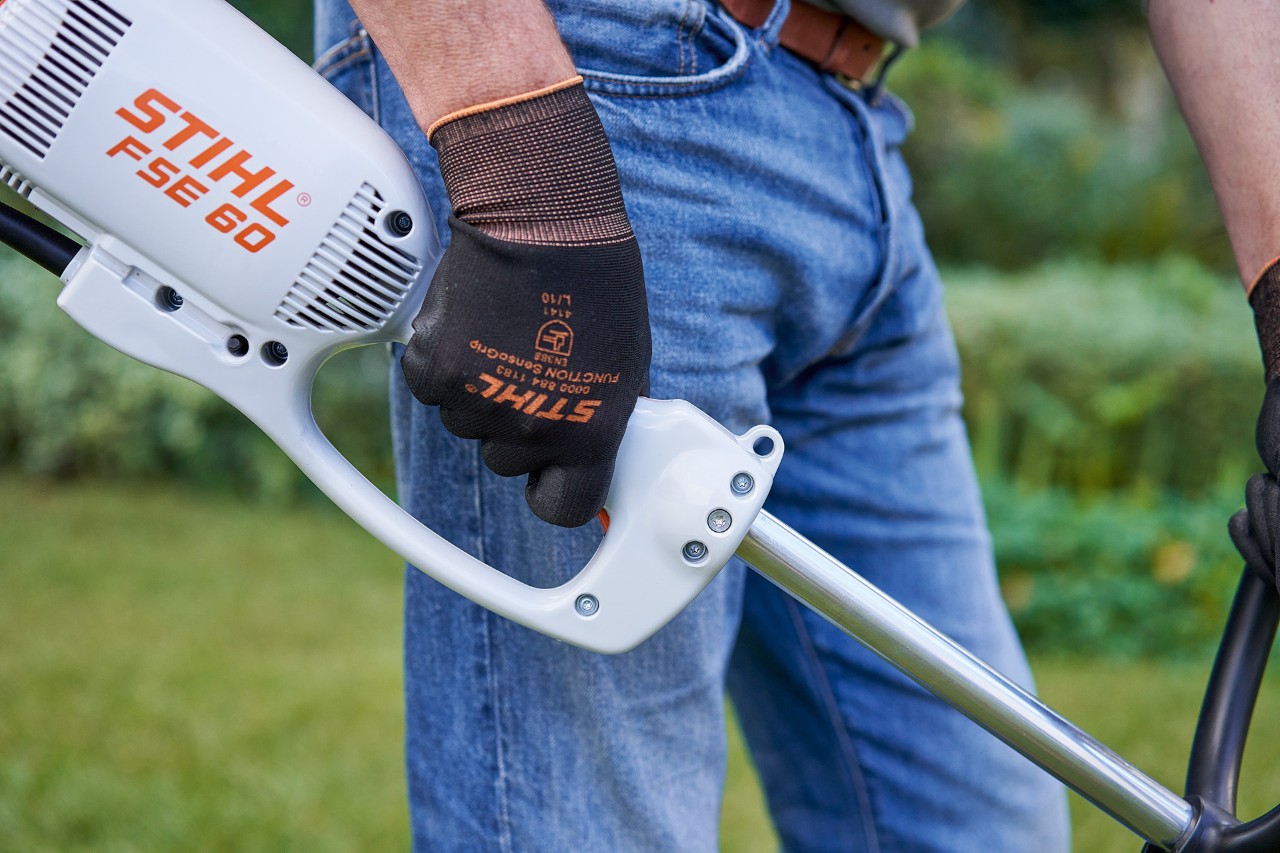 Burri duke shtypur butonin në dorezën e kontrollit të një motokose STIHL FSE 60