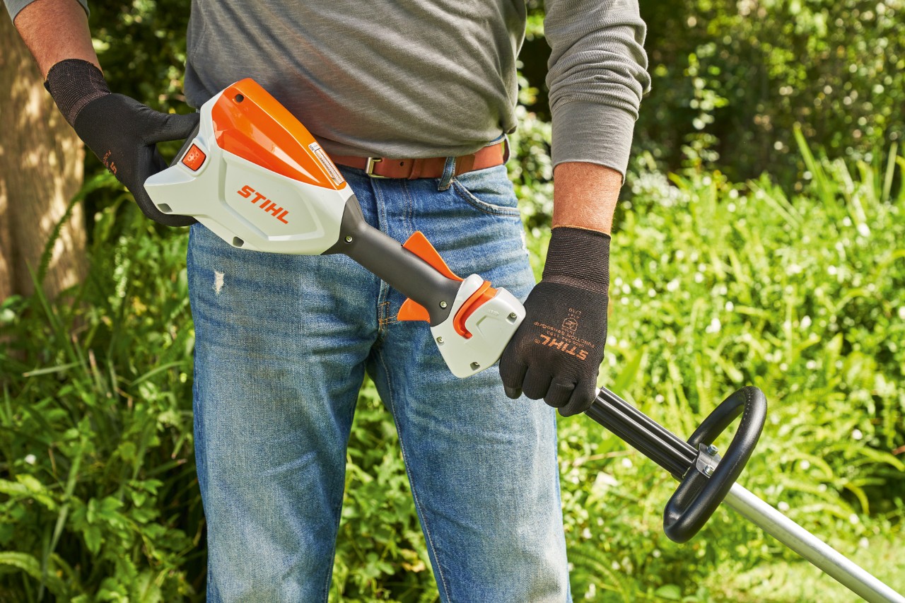 Një burrë që mban doreza mbrojtëse duke kontrolluar baterinë e kositëses pa kabllo STIHL FSA 60 përpara se ta ndezë atë.