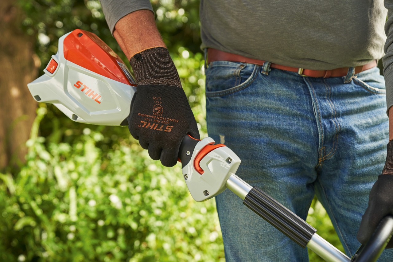 Një burrë që mban doreza mbrojtëse duke shtypur këmbëzën e komandimit të motokosës pa kabllo STIHL FSA 60 për ta vënë në funksionim