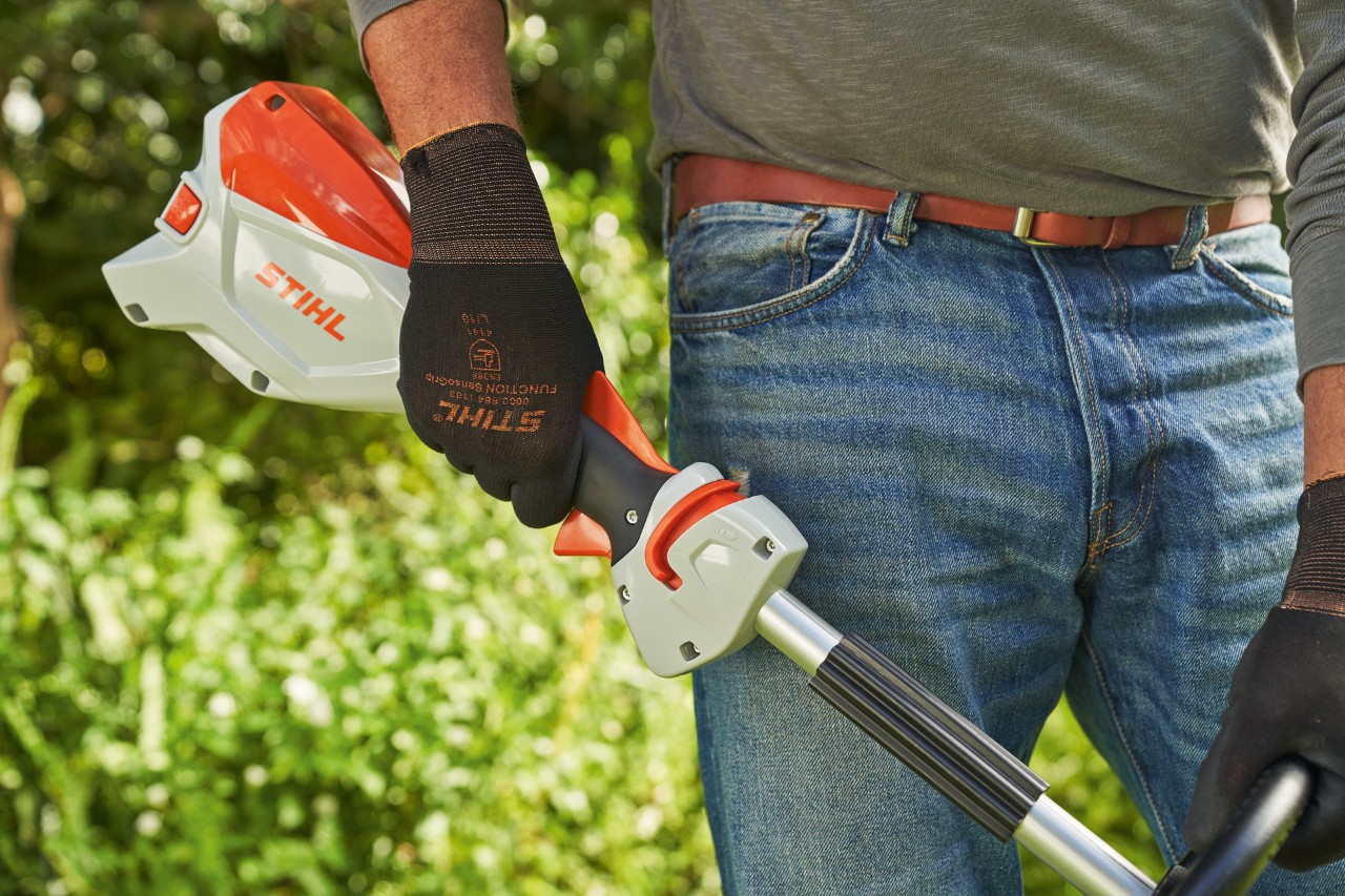 Një burrë që mban doreza mbrojtëse duke lëshuar këmbëzën e motokosës pa kabllo STIHL FSA 60 për ta fikur atë.