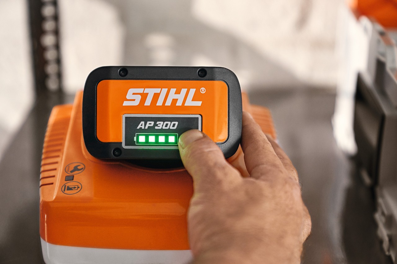 Person umfasst das STIHL Schnellladegerät mit Lithium-Ionen-Akku AP 300, um den Ladestand zu kontrollieren